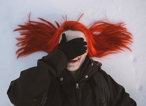 A woman with red hair covering her face in the snow