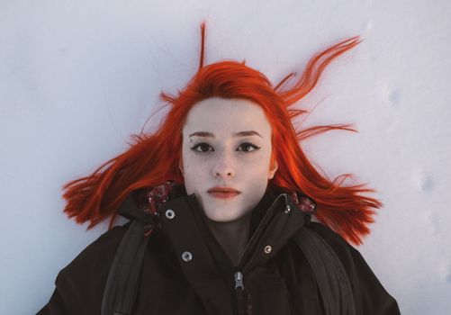 Portrait of a redhead woman with freckles lying on snow in a winter setting.