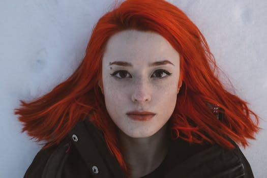 Vibrant red-haired woman lying on snow, showcasing freckles and dramatic makeup.