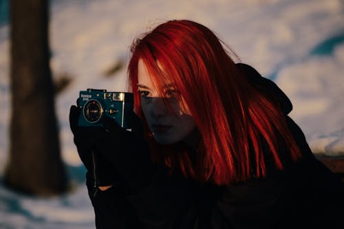 A woman with red hair taking a picture with a camera