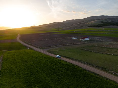A picturesque view of a rural farm landscape surrounded by fields and mountains at sunset.