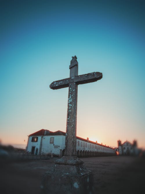 A cross in front of a building at sunset