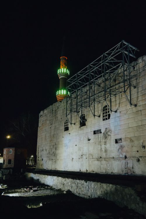 Free A mosque's glowing minaret casts colorful reflections on a historic wall at night. Stock Photo