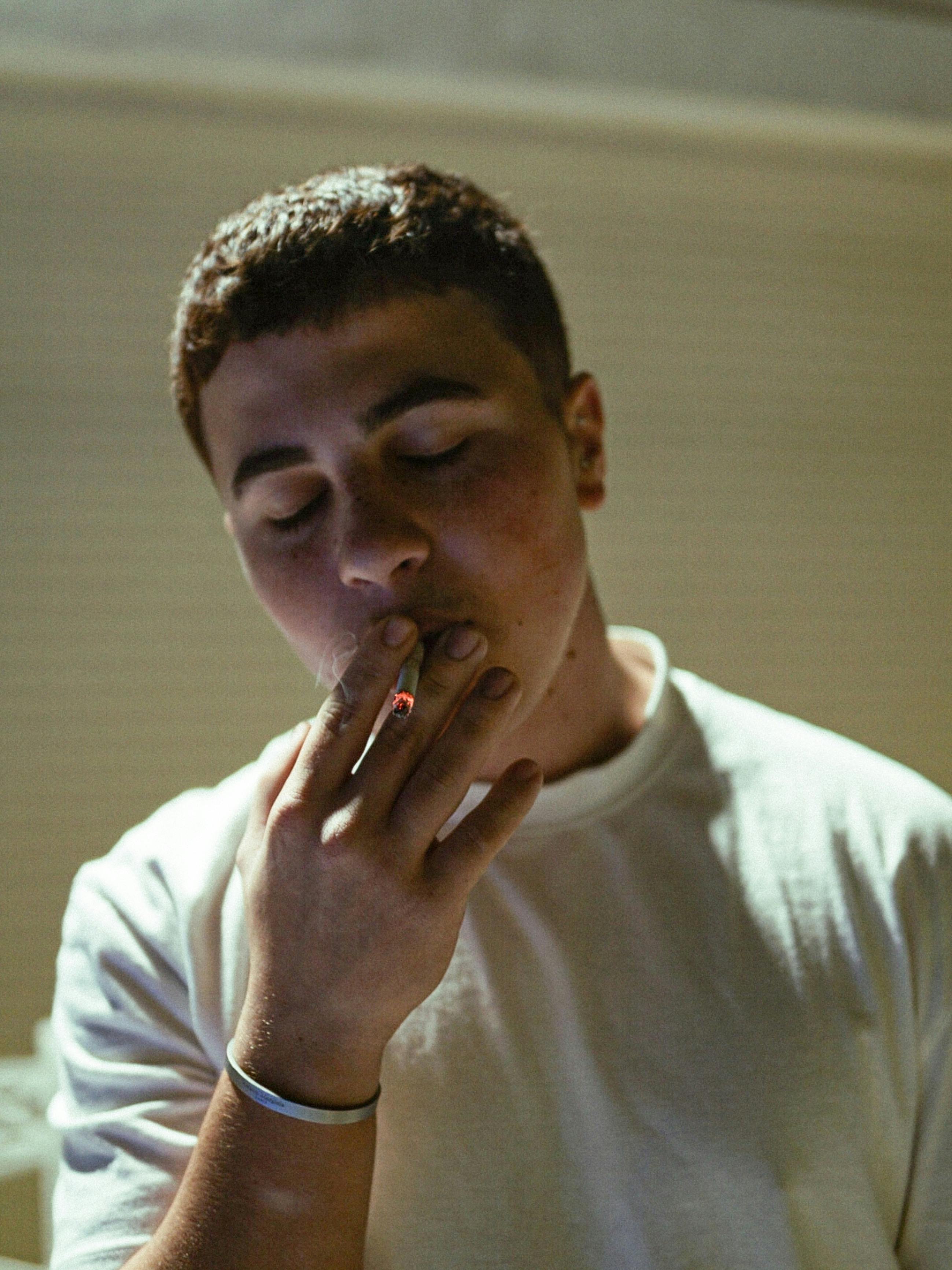 A portrait of a young adult male smoking indoors with eyes closed, conveying relaxation.