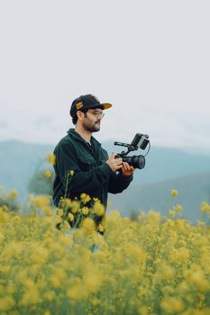 A man takes photos in a yellow-flowered rural meadow, showcasing nature's beauty.