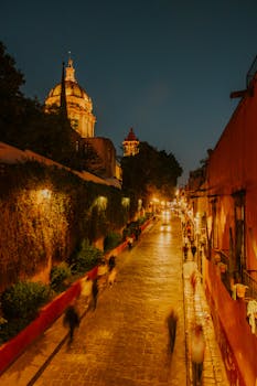 Blurred pedestrians walk along an illuminated street in San Miguel de Allende at twilight.