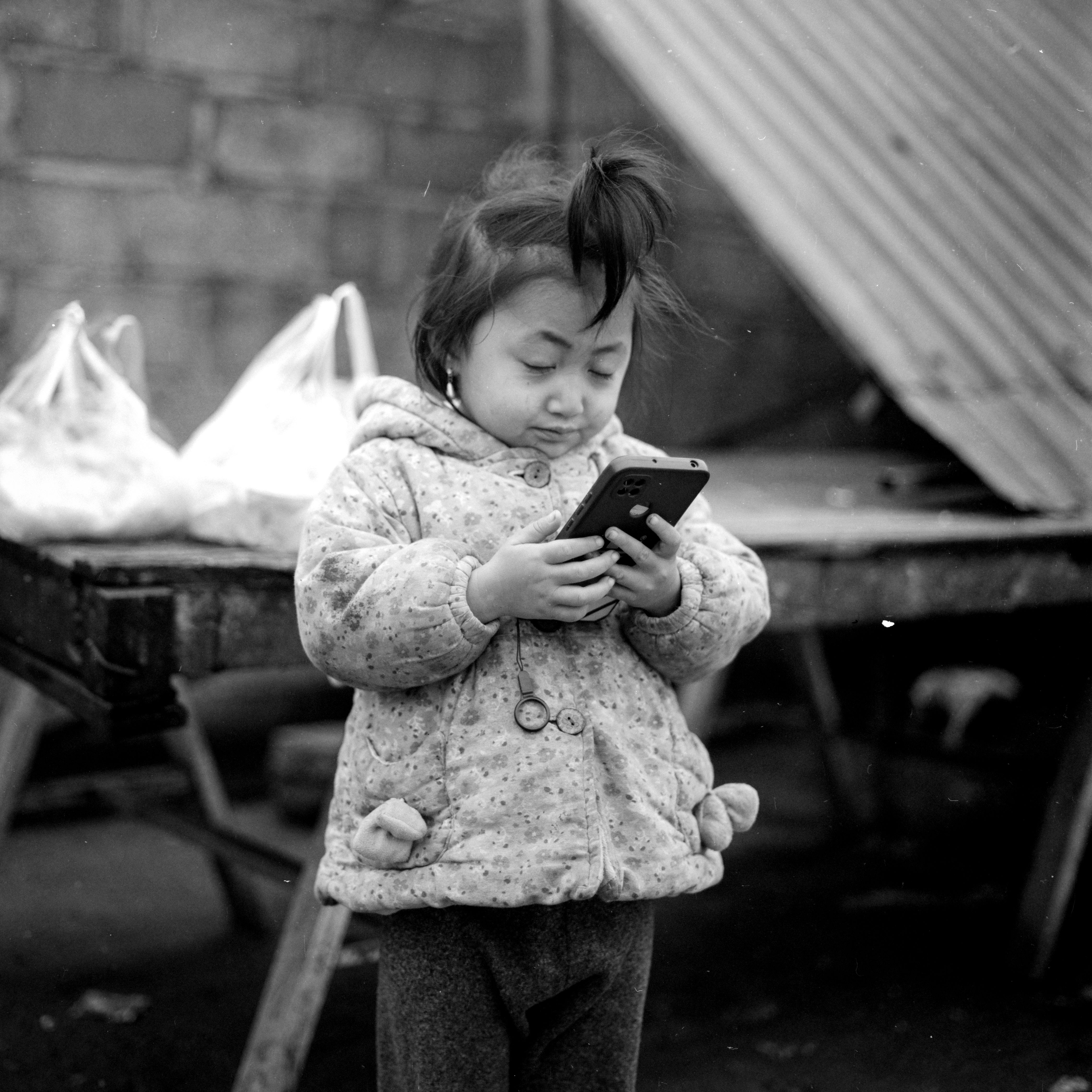 Black and White Photo of a Little Girl Holding a Smartphone 