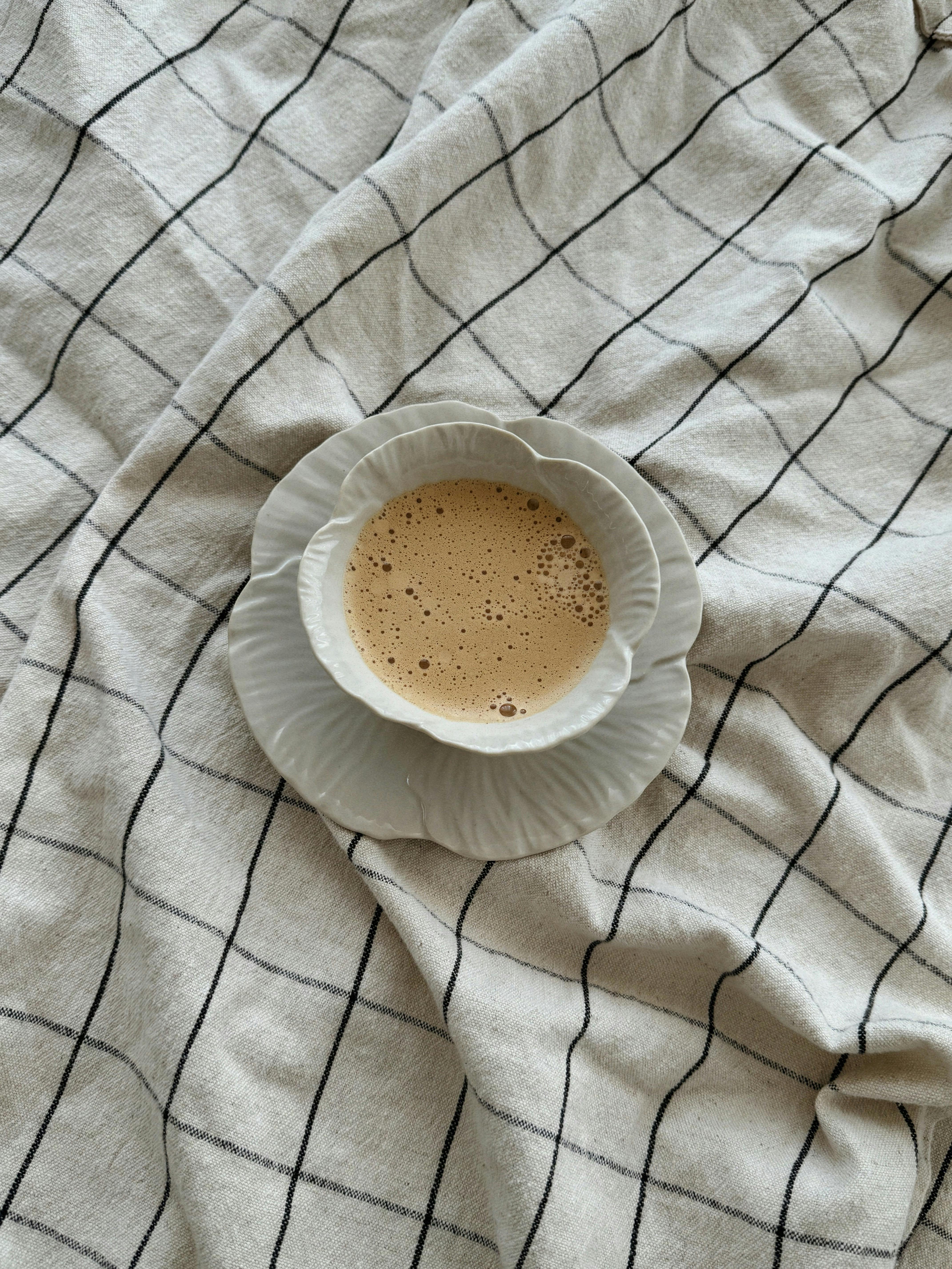 A top view of a coffee cup on checkered bed linen, creating a cozy morning vibe.