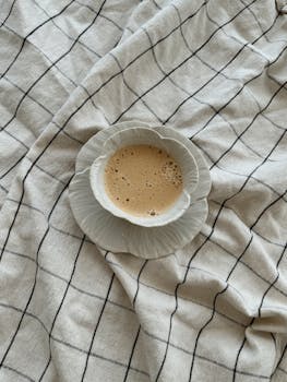 A top view of a coffee cup on checkered bed linen, creating a cozy morning vibe.