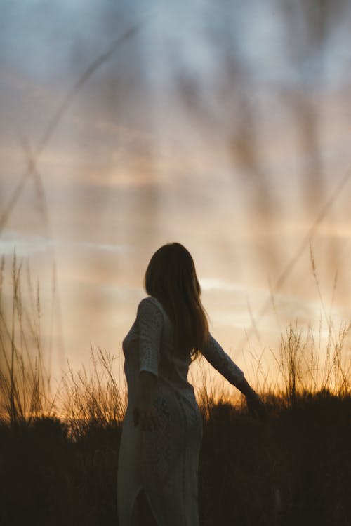 A woman standing in tall grass at sunset