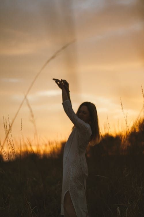 A woman in a field holding up a kite at sunset