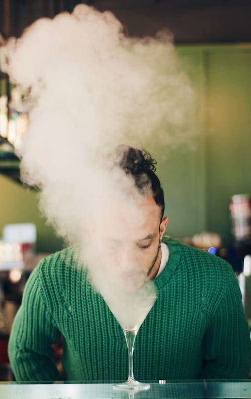 A man in green sweater smoking a cocktail