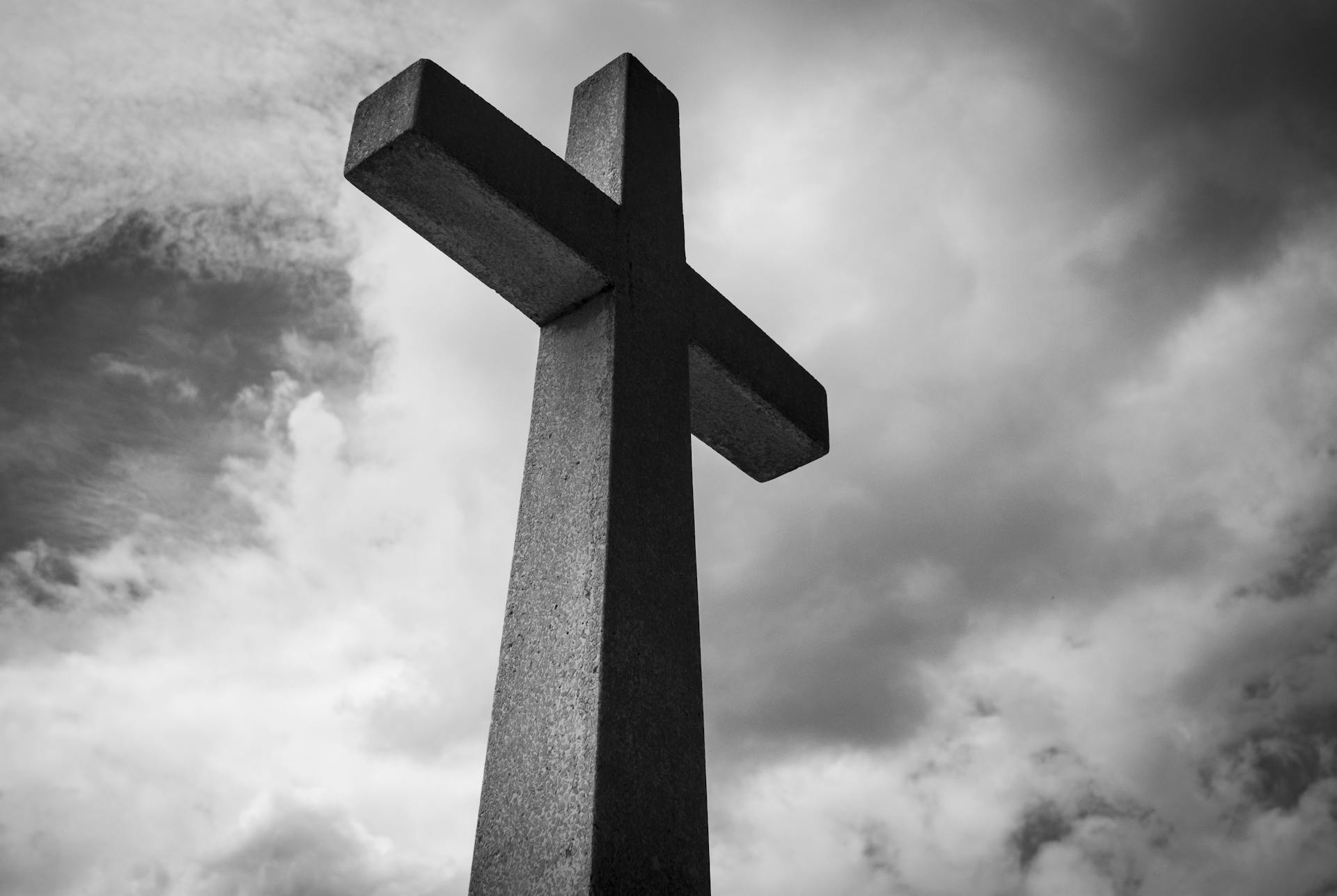 A black and white photo of a cross set against a dramatic, cloudy sky, symbolizing spirituality and faith.