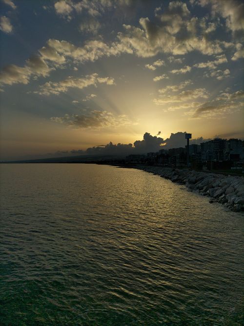 Free Captivating sunset view over Erdemli's shoreline in Mersin, Türkiye, showcasing the serene ocean and city silhouette. Stock Photo