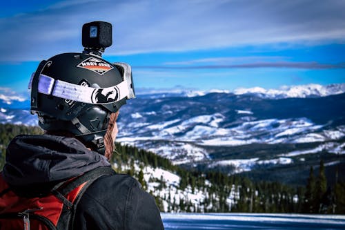 Man in Helmet With Action Camera Looking at Snow Mountain