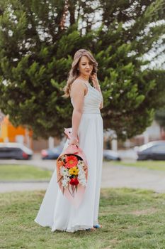 Bride in a white dress holding a floral bouquet, standing outdoors.