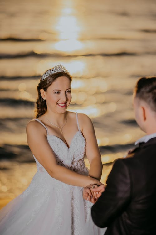 A bride and groom standing on the beach at sunset