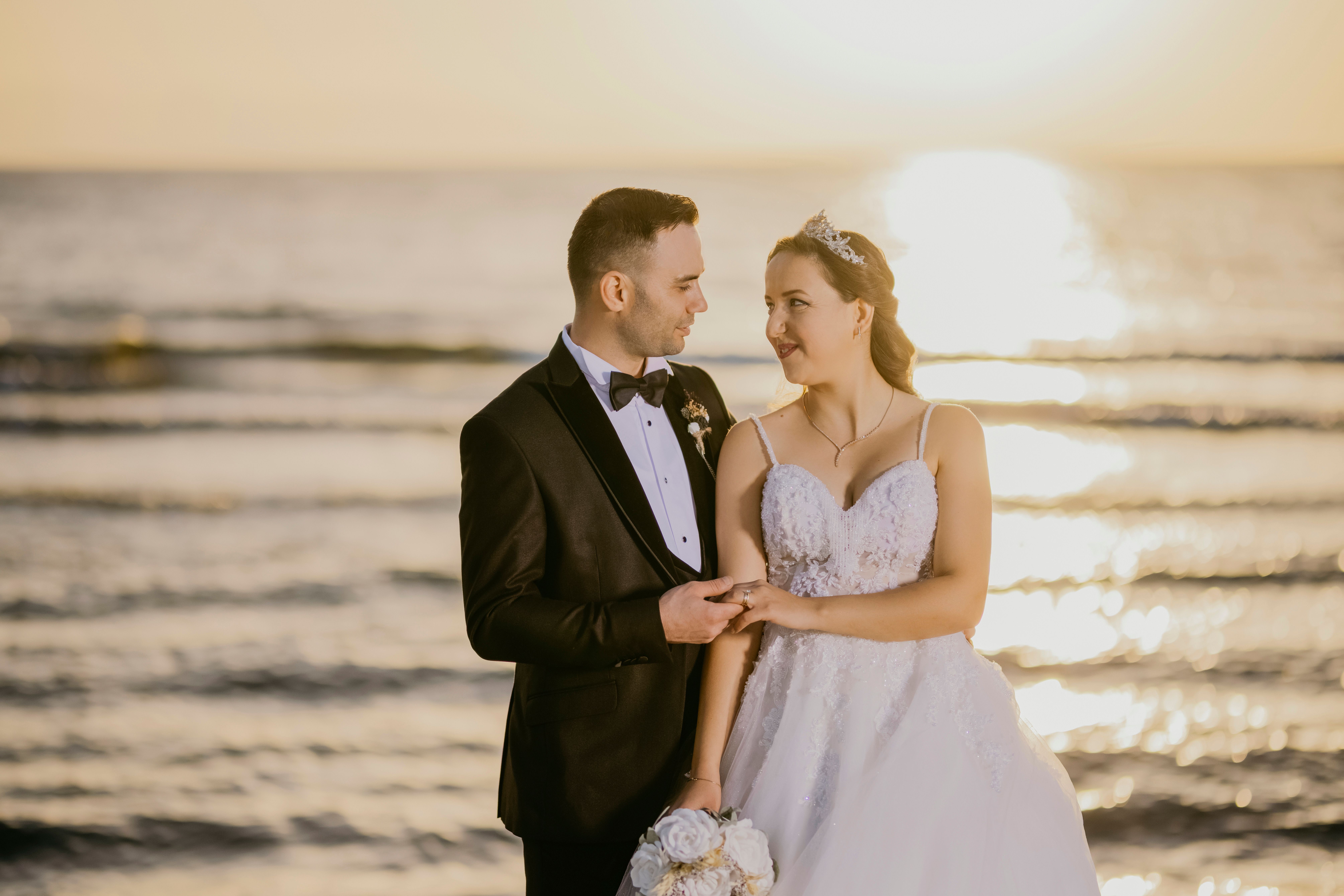 Couple in wedding attire embracing by the sea at sunrise, exuding love and romance. - Photo by Mehmet DEMİR on Pexels