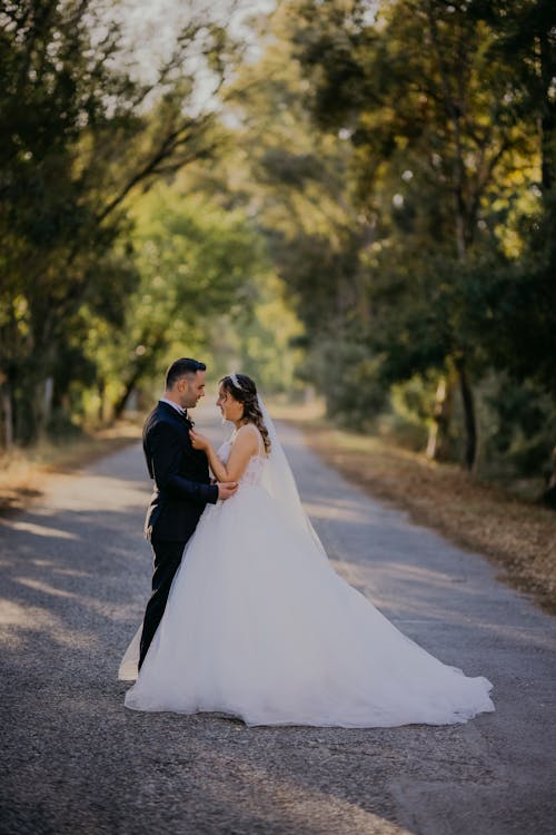 A bride and groom standing on a road in the woods