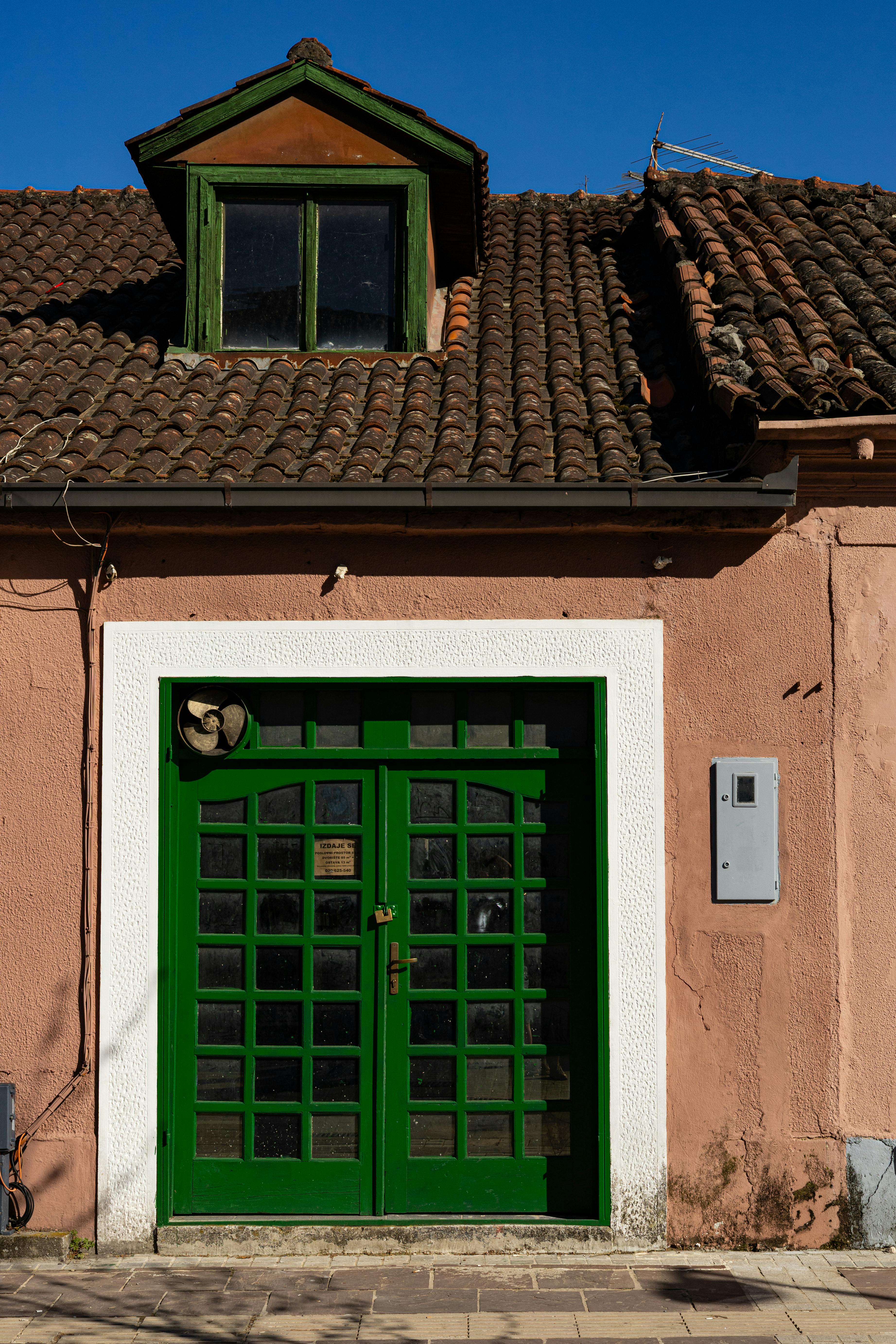 Explore this rustic townhouse facade with vibrant green double doors and a classic tiled roof.