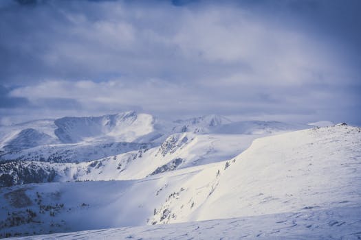Expansive view of a snow-covered mountain range under dramatic cloudy skies, capturing winter's serene beauty.