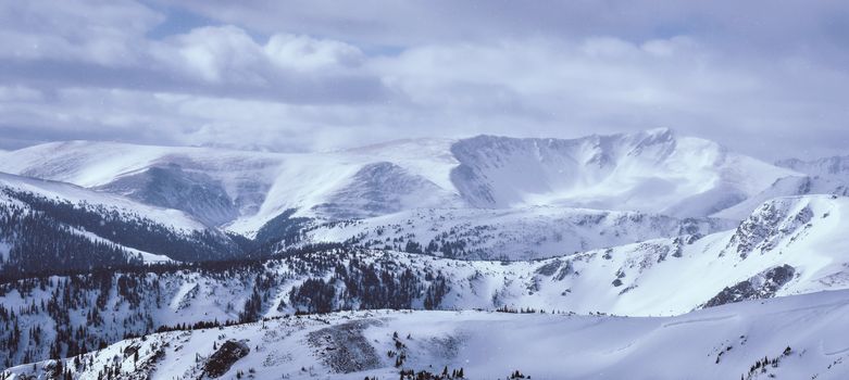 A breathtaking view of snow-capped mountains under a cloudy winter sky, showcasing natural beauty.