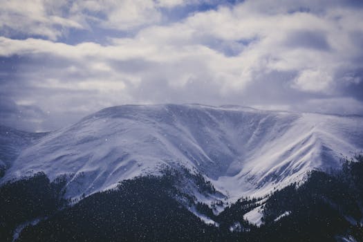 Stunning snow-covered mountain under a dramatic cloudy sky, capturing winter's serene beauty.