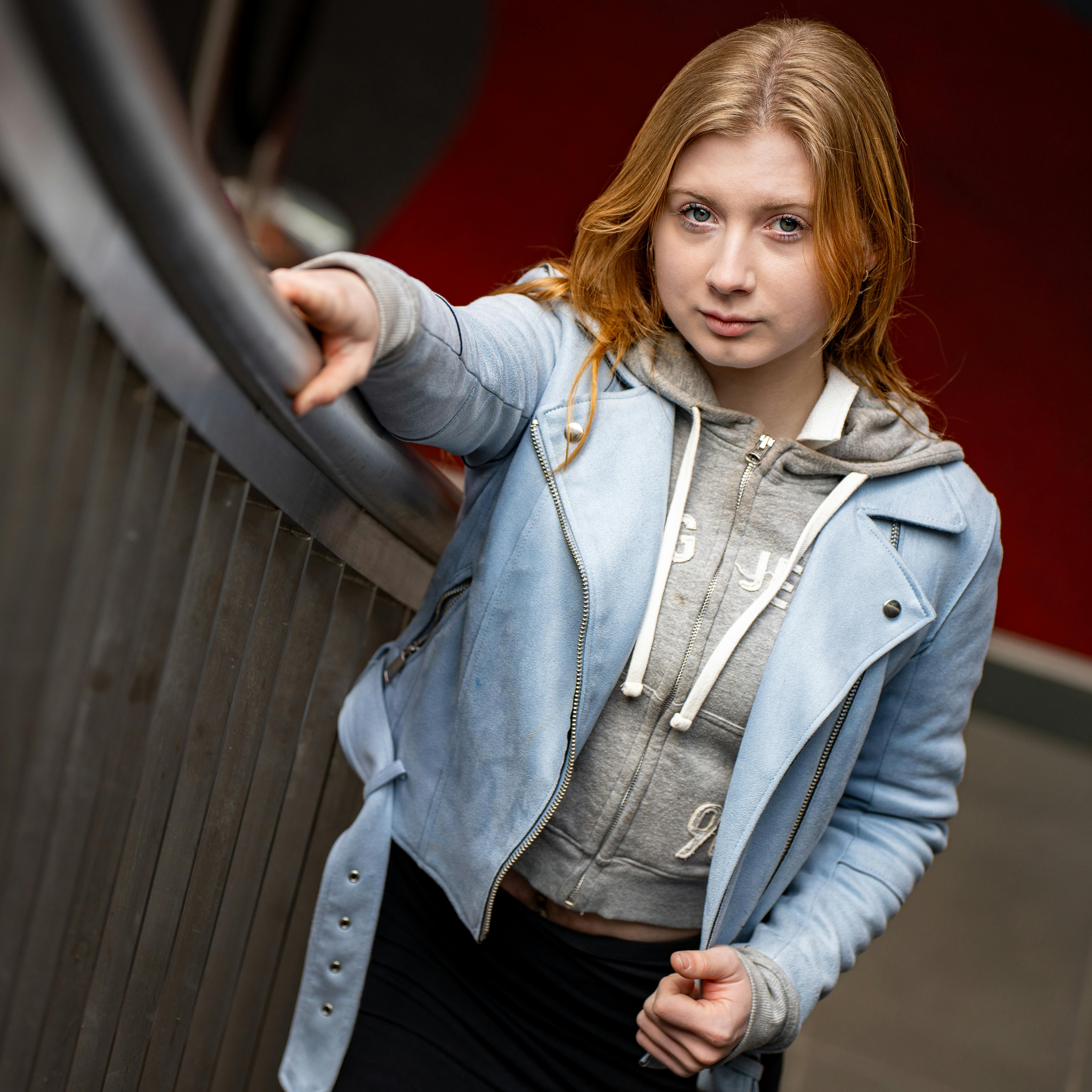 Stylish young woman in denim jacket and hoodie posing confidently indoors.