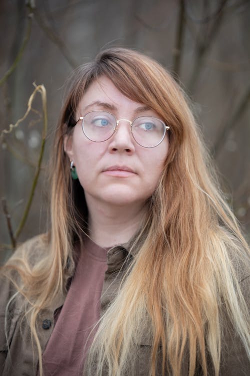 A woman with glasses and brown jacket standing in the woods