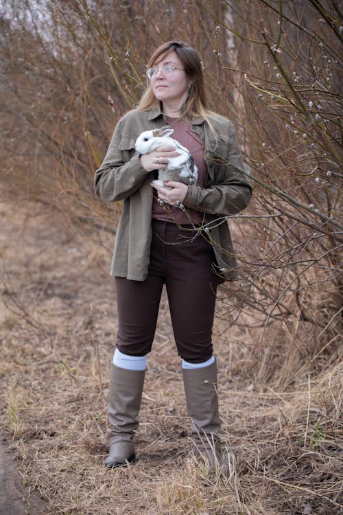 A woman in brown pants and brown boots holding a rabbit