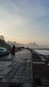 A misty morning scene with a cyclist on a seaside promenade, enveloped by fog.