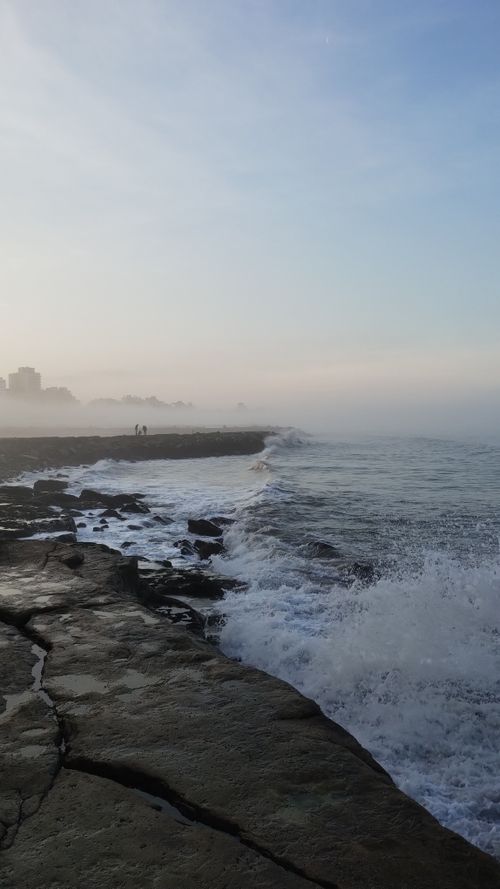 Free A misty seascape with waves crashing against a rocky breakwater under a soft, overcast sky. Stock Photo