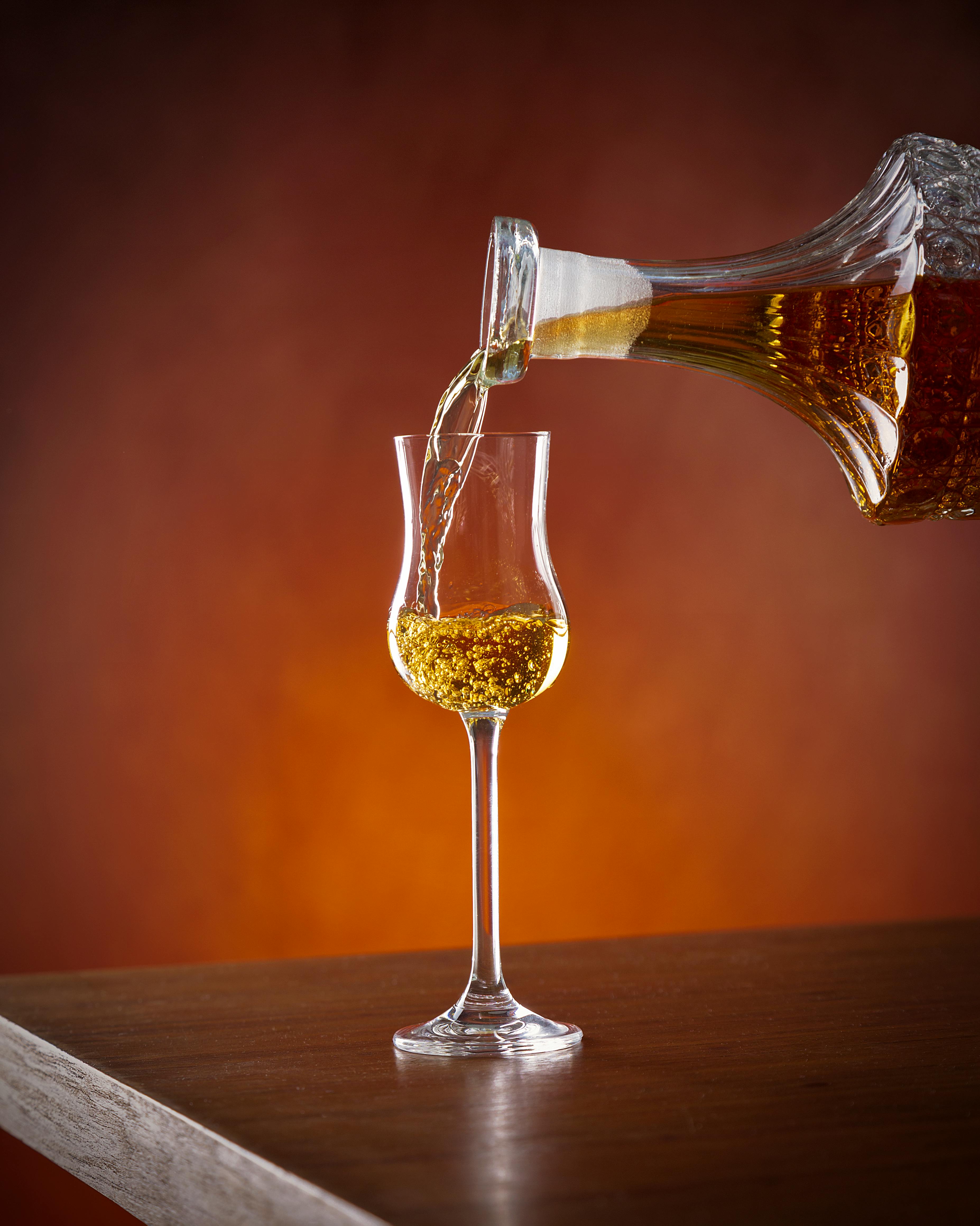 Crystal decanter pouring amber liquor into a wineglass against a warm background.
