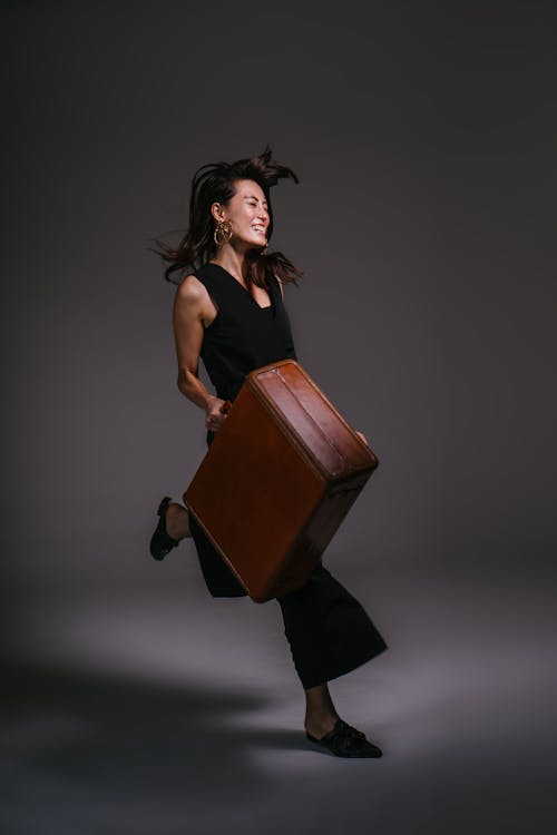 Photo of Smiling Woman Running While Holding Brown Leather Suit Case