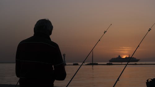 A man fishing at sunset with a cruise ship in the background