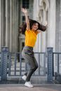 Photo of Smiling Woman in Yellow T-Shirt and Grey Pants With Her Hands Raised
