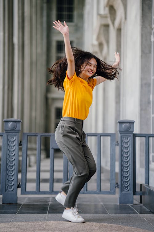 Free Photo of Smiling Woman in Yellow T-Shirt and Grey Pants With Her Hands Raised Stock Photo