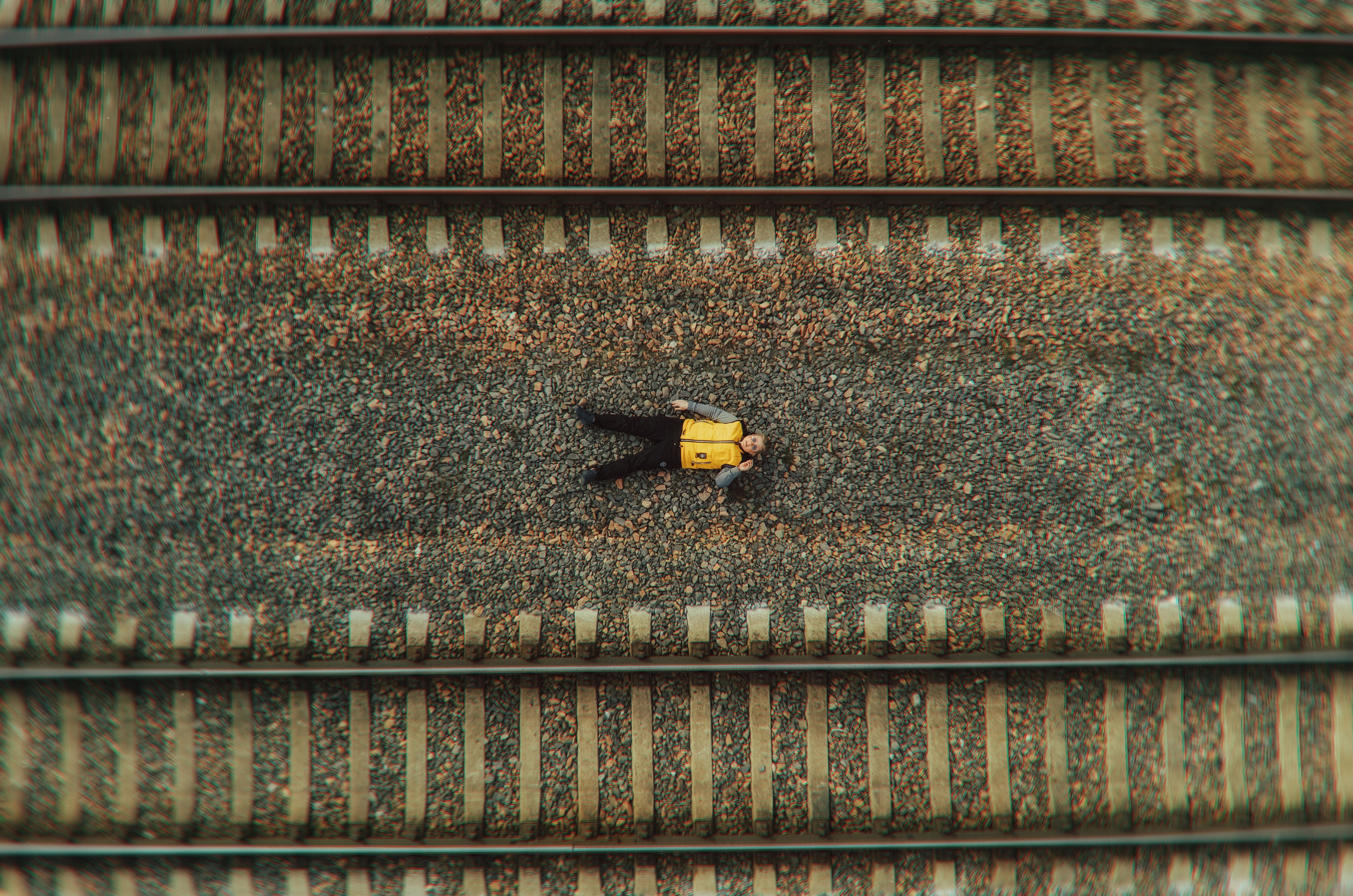 Aerial shot of a man in yellow jacket lying on railway tracks, creating a unique perspective.