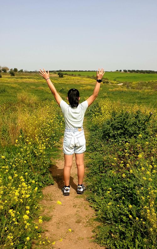 Free A woman stands with arms raised in a vibrant meadow, embracing nature's beauty in the countryside. Stock Photo
