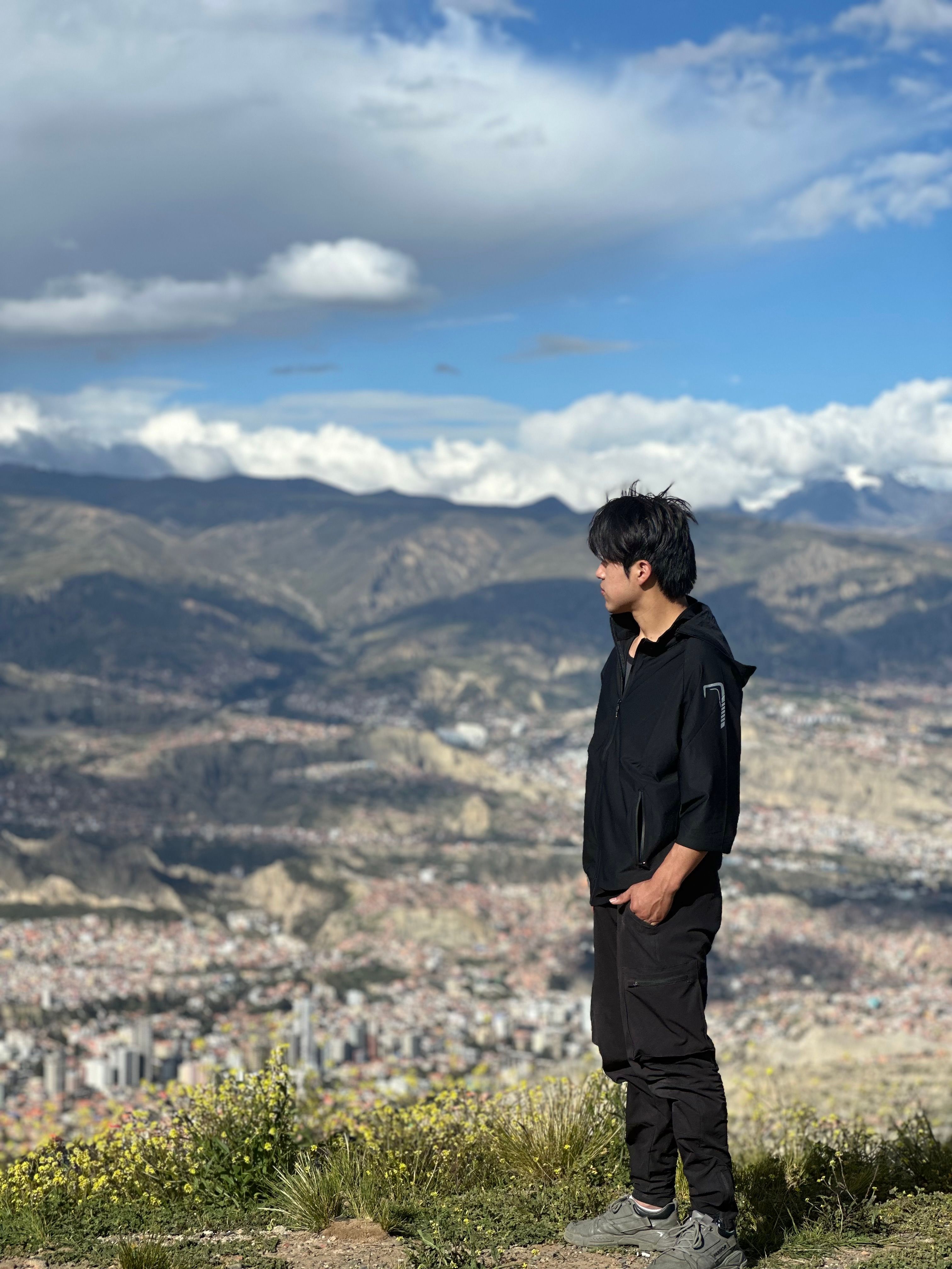 A man stands on a hill overlooking a mountain landscape with a sprawling city below.