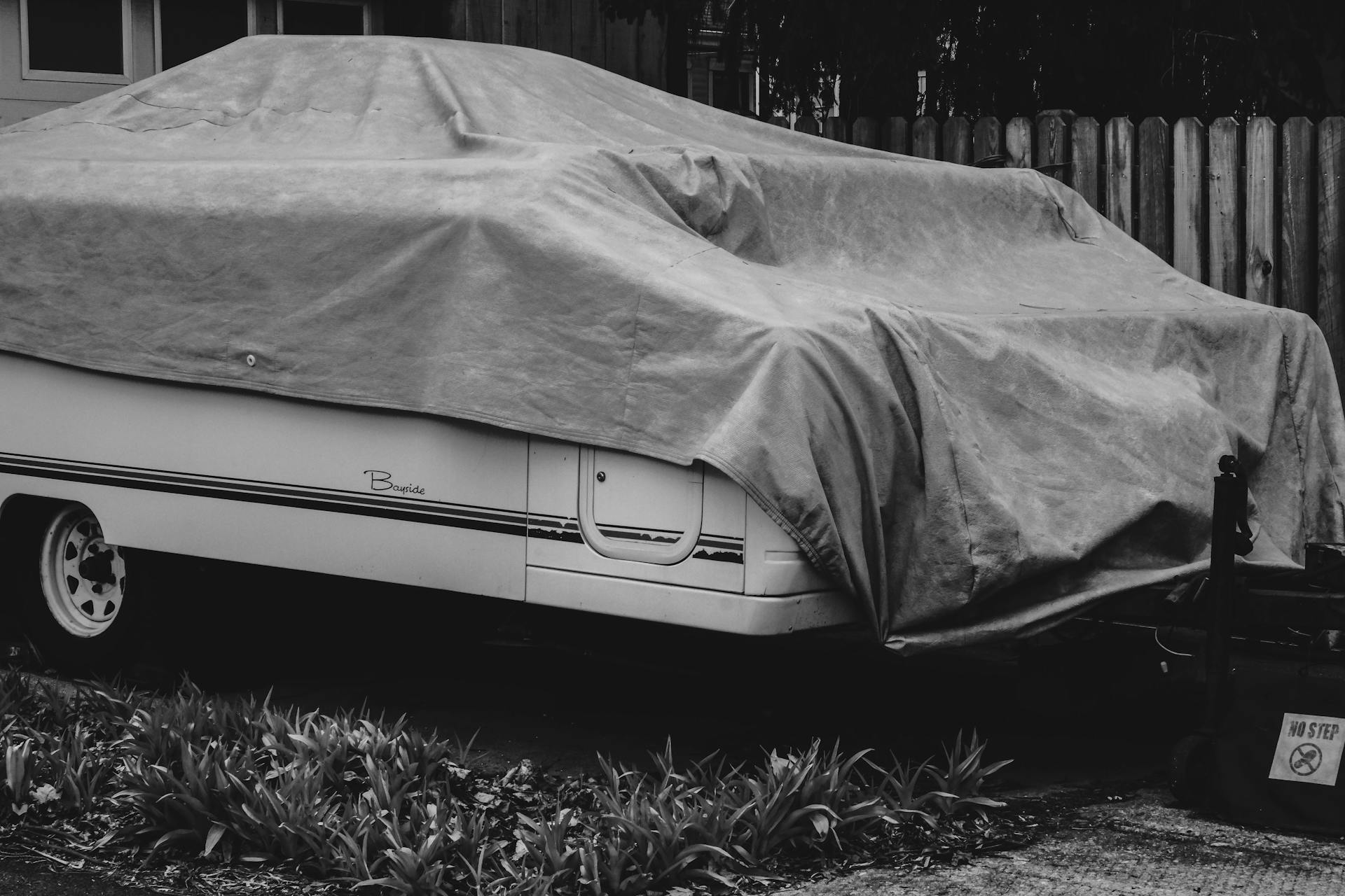 Black and white photo of a camper trailer covered with a tarp in a rural area.