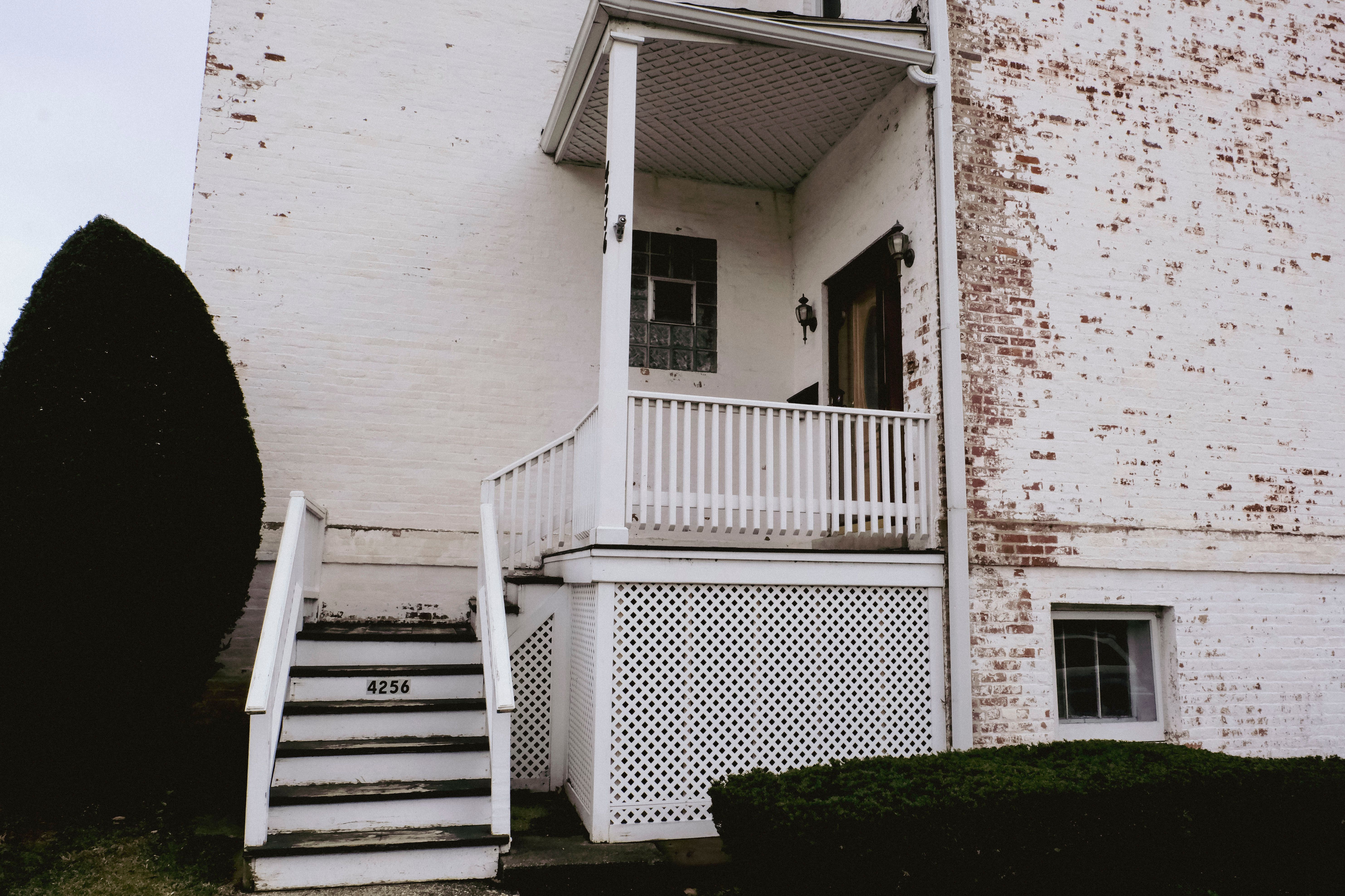 A rustic white brick house entrance with stairs and porch, accented by greenery.