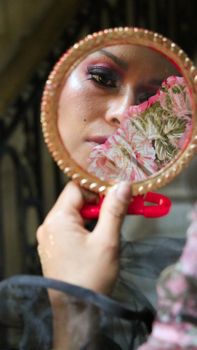 A close-up of a woman holding a floral mirror reflecting her face against an outdoor backdrop.