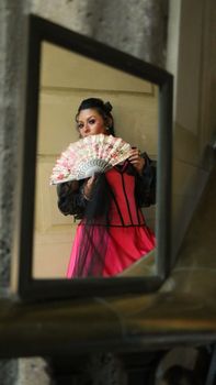 Portrait of a woman holding a fan, reflected in a mirror, wearing traditional attire.