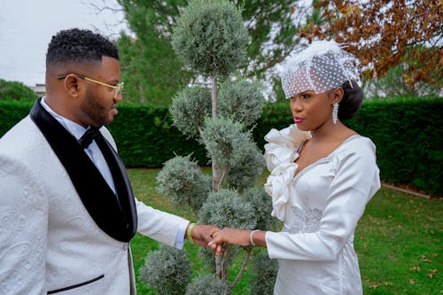 A man and woman in white wedding attire holding hands