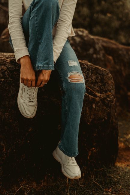 A person in ripped jeans and sneakers sits on a rock outdoors. Casual and stylish vibe.