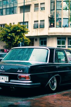 Classic black Mercedes parked in city street with wet asphalt.
