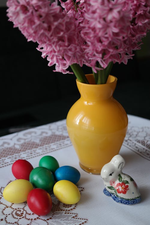 Easter Eggs, an Easter Bunny and a Vase with Pink Blooming Flowers Standing on a White Tablecloth