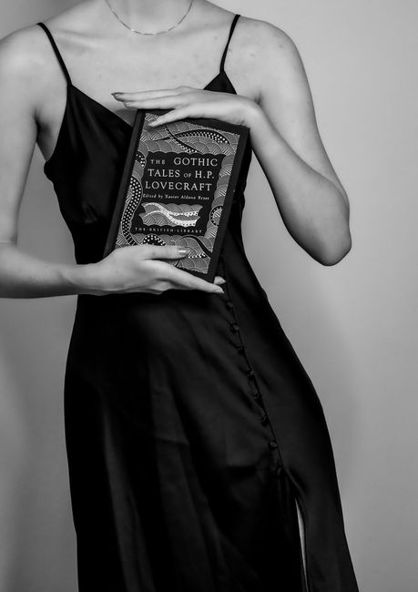 Black and white image of a woman in a dress holding an H.P. Lovecraft book, capturing a gothic mood.