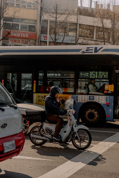 Free A motorcyclist waits in urban traffic alongside a city bus on a busy street. Stock Photo